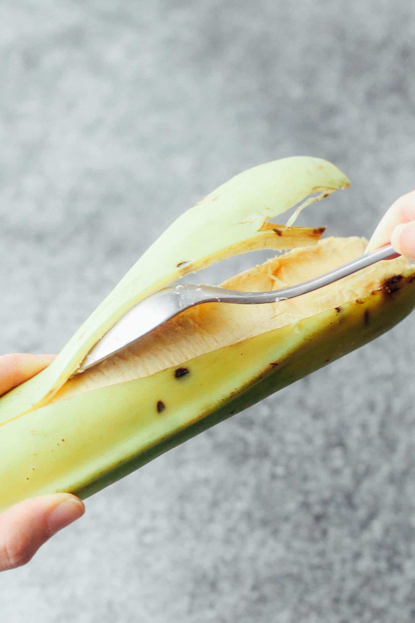 A plantain being peeled with a spoon