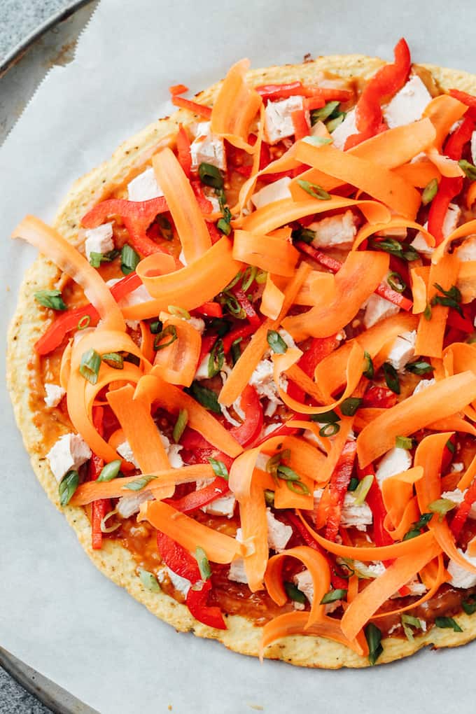 Thai Chicken Pizza with Cauliflower Crust | Destination Delish - Just in time for pizza night! A healthy, Thai inspired pizza with colorful, crunchy veggies, chicken, and a tangy peanut sauce atop cauliflower crust. 