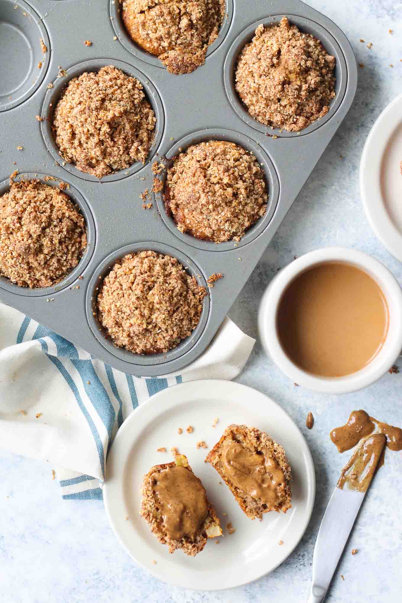 Muffins in the tin with a cup of coffee and almond butter spread on a single muffin