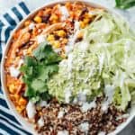 Easy salsa chicken in a bowl with quinoa and lettuce, and topped with guacamole, sour cream, and cotija cheese