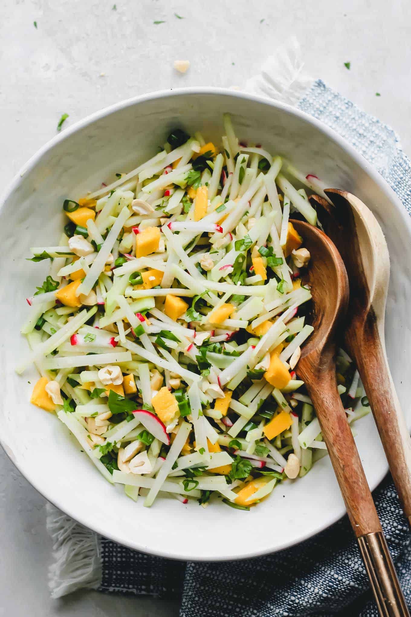 Tossed kohlrabi salad in a white bowl with salad servers.
