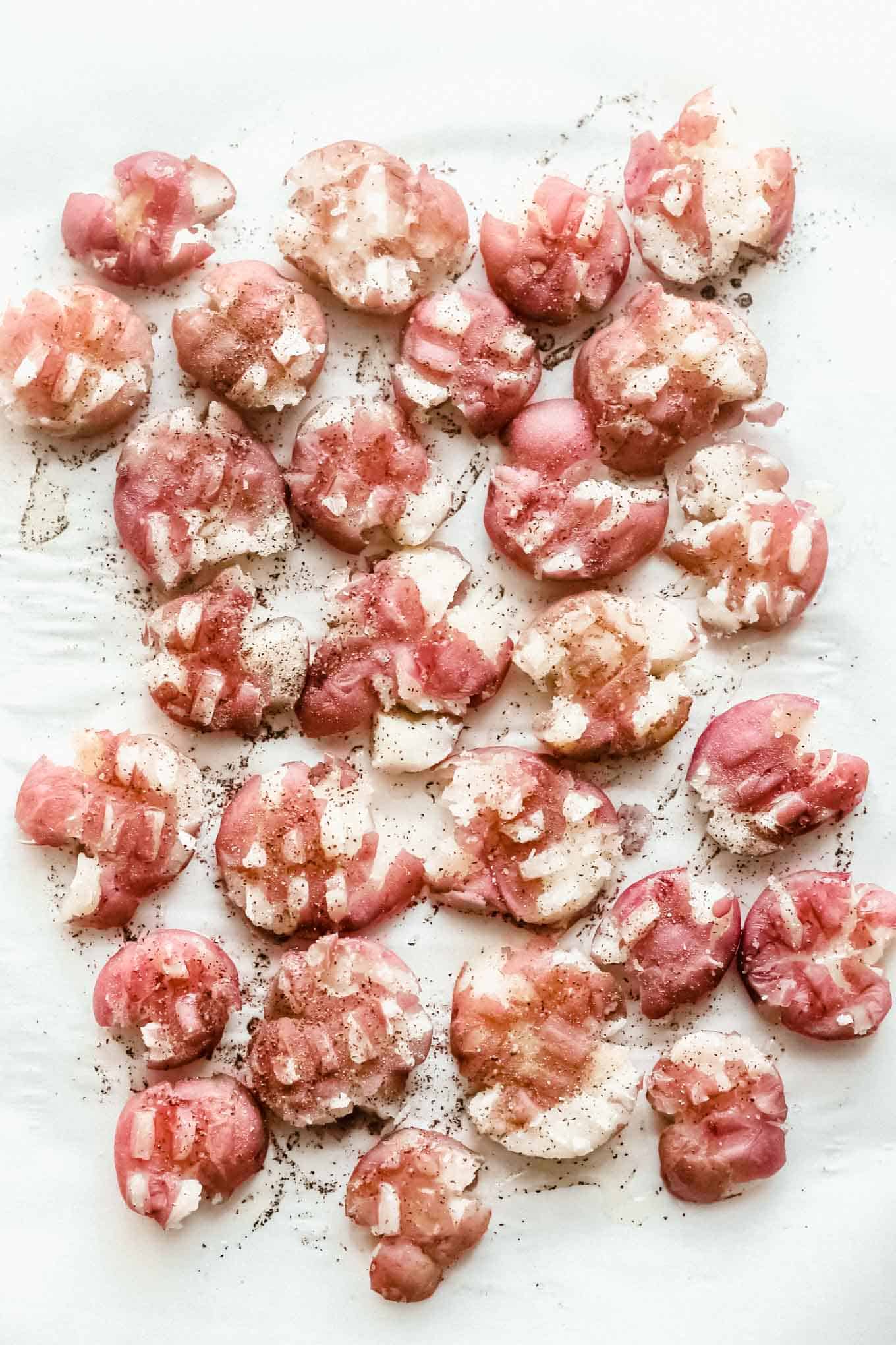 Smashed red potatoes on parchment paper prior to grilling