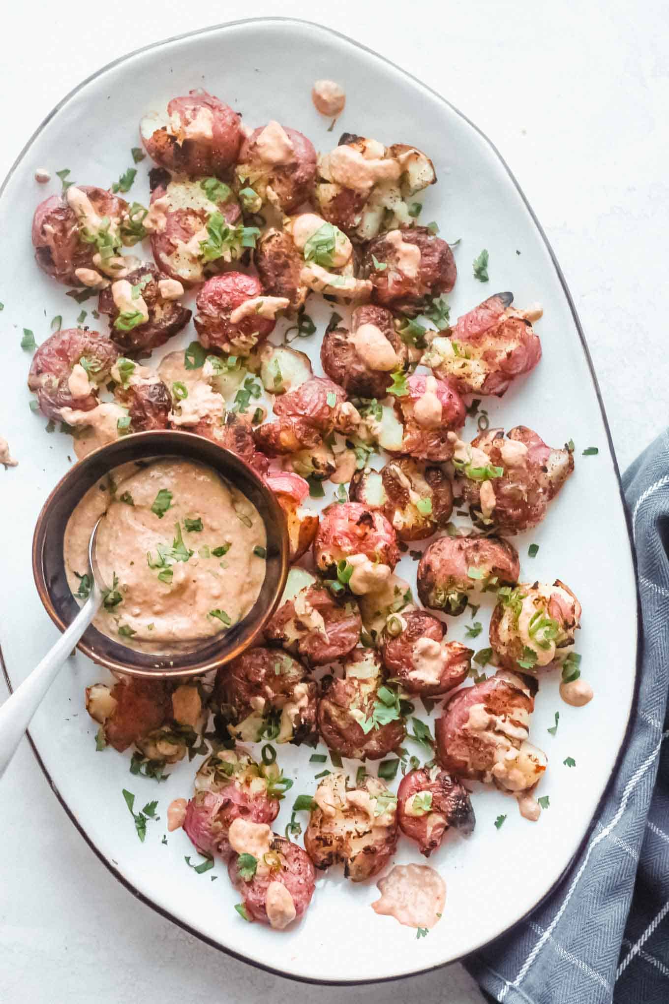Grilled smashed potatoes on a large platter with dipping sauce on the side 