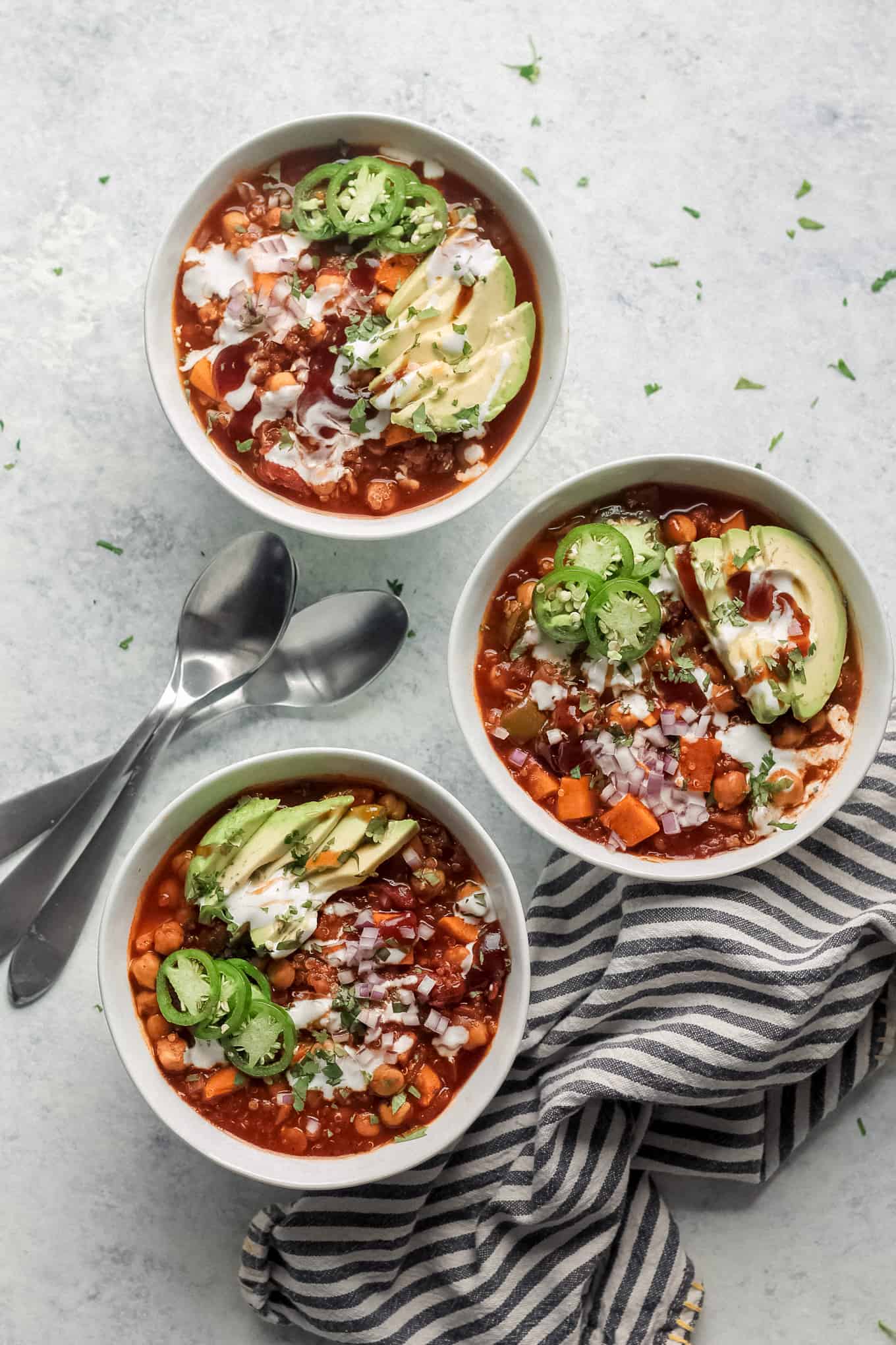 Chili in white bowls topped with avocado and jalapeno slices, red onion, sour cream, BBQ sauce, and chopped cilantro