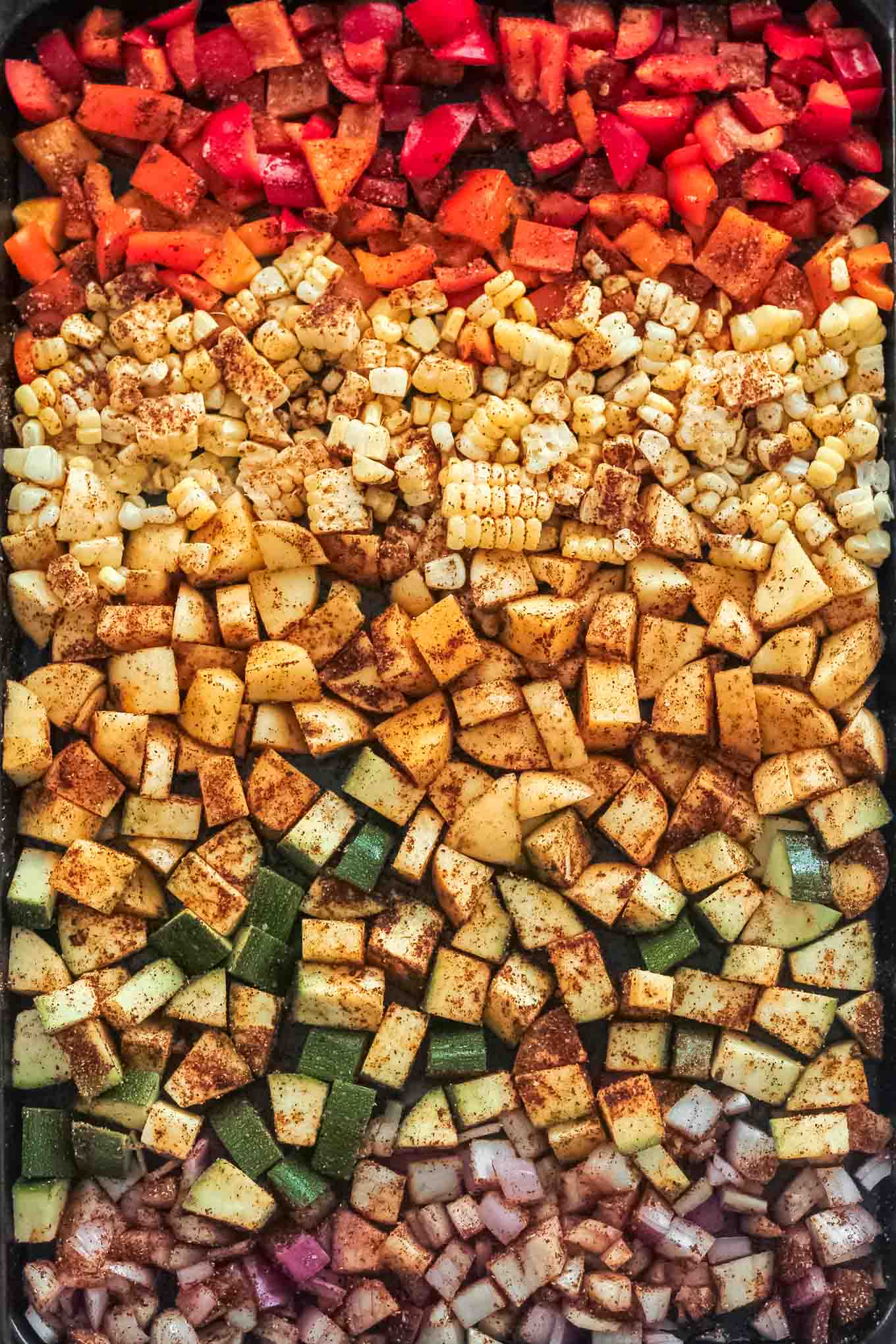 The sheet pan of peppers, zucchini, corn, and potatoes before roasting