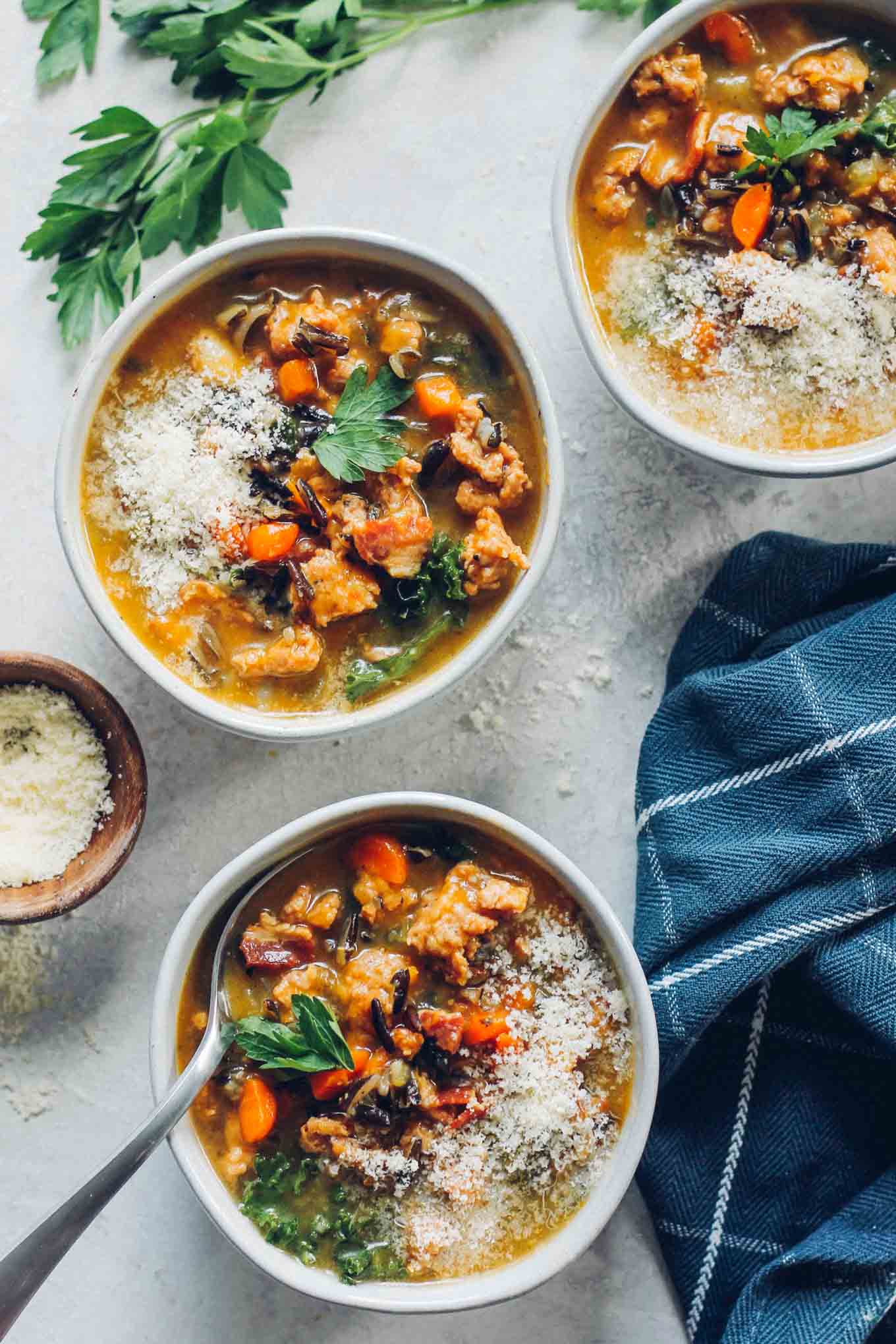 Soup in 3 bowls with parmesan cheese and parsley on the side