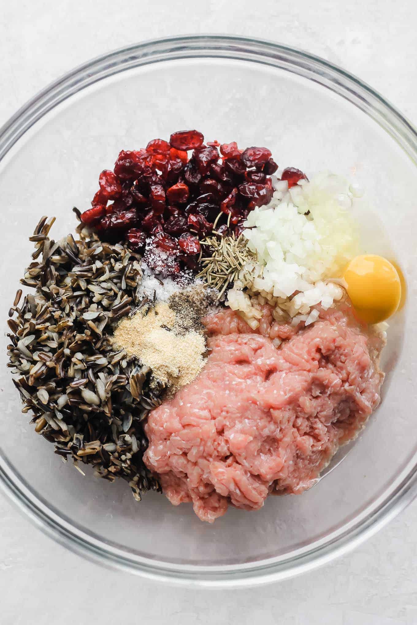 Raw ground turkey, wild rice, cranberries, and seasonings in a bowl before mixing