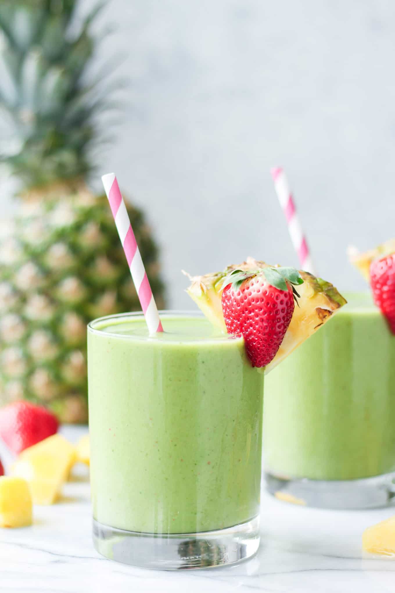 A close up view of the Tropical Island Green Smoothie in a glass with a strawberry and pineapple slice decorating the rim.