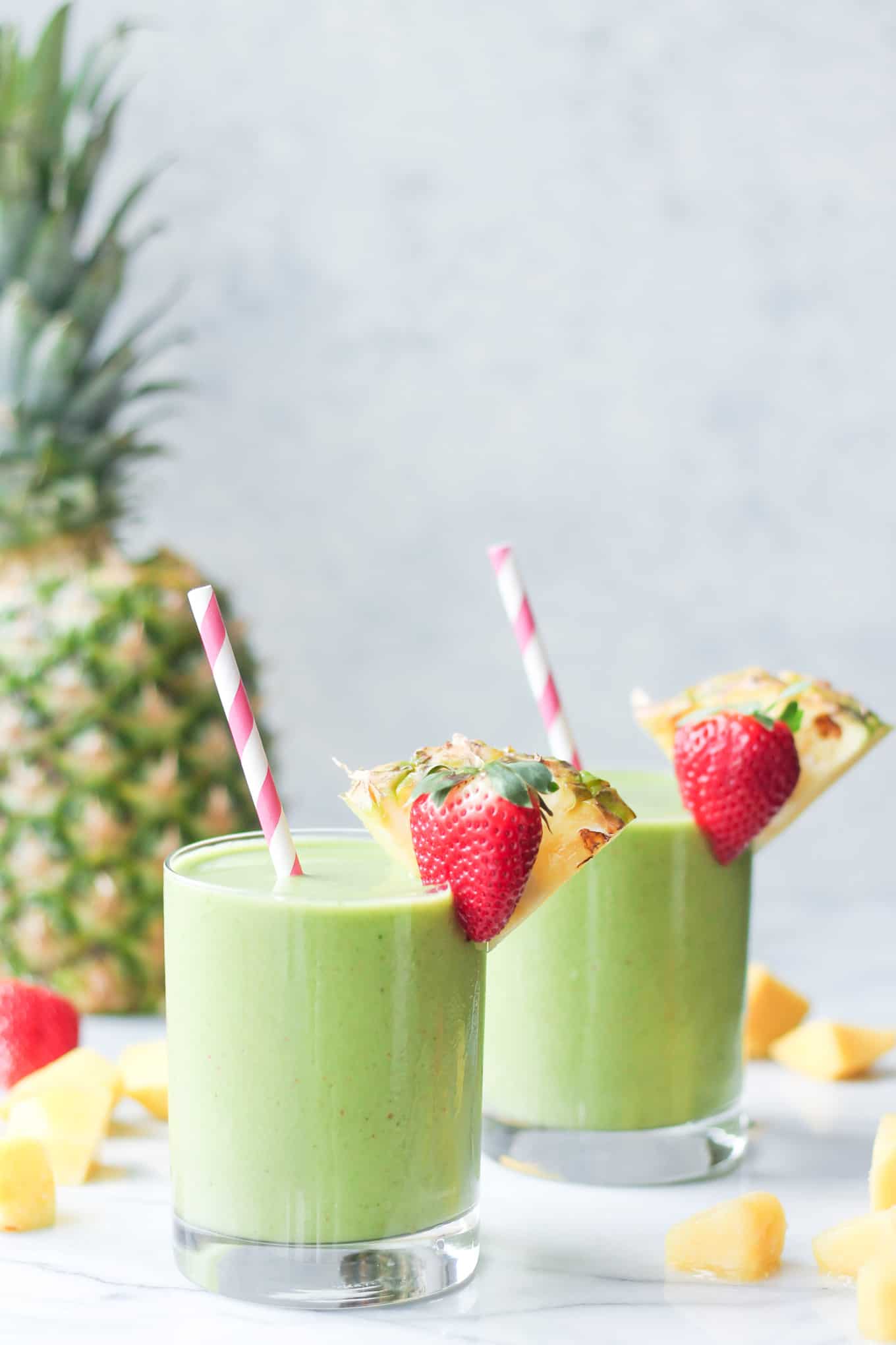 Two Tropical Island Green Smoothies in glasses with a strawberry and pineapple slice decorating the rims.