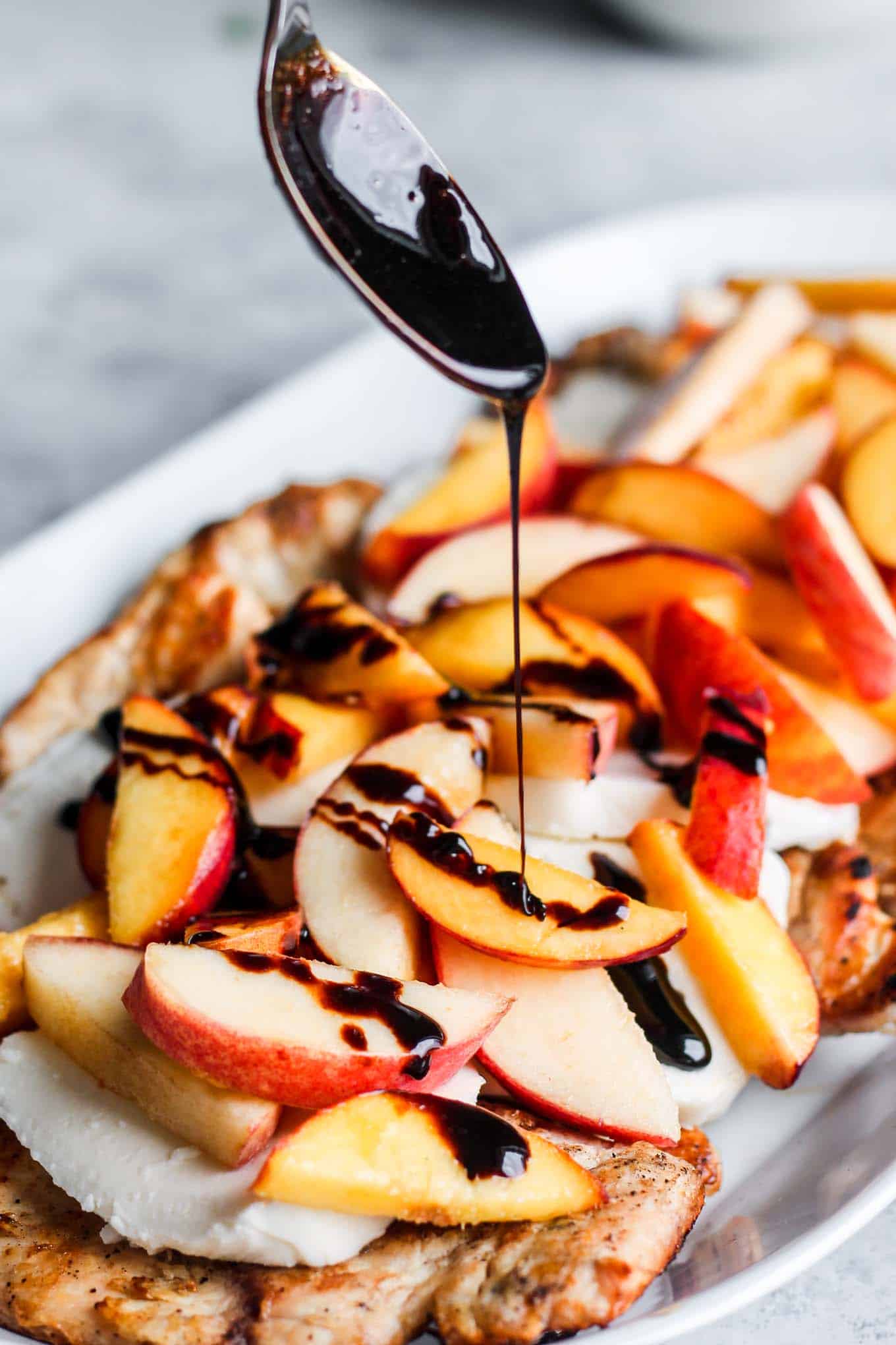 A spoon drizzling the balsamic glaze over the peach caprese grilled chicken.